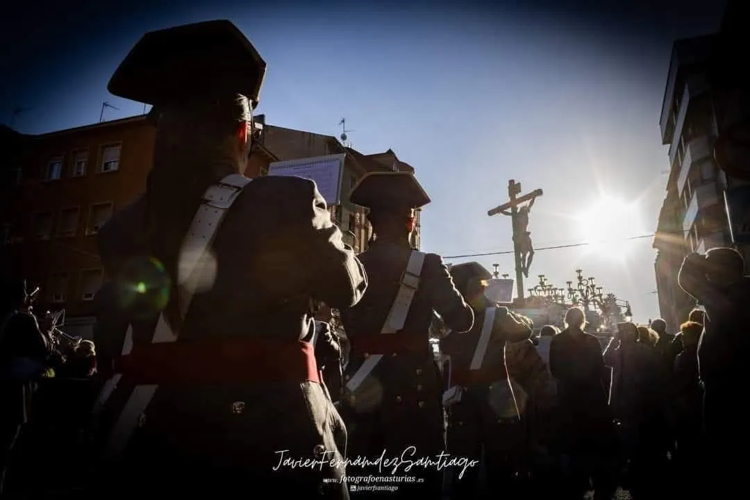 La formación toca a contraluz en una mañana despejada, con el paso del Crucificado al fondo.