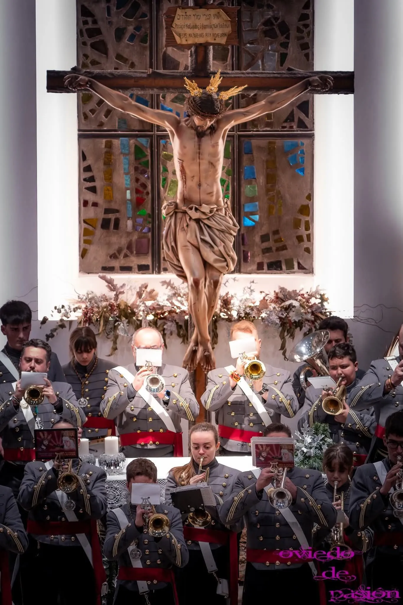 La agrupación toca en el interior de una capilla, con músicos de todas las edades leyendo sus partituras.
