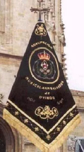 El banderín desplegado en su mástil ante una fachada de piedra, con el bordado en oro sobre terciopelo negro.