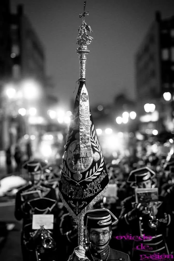 El banderín de la agrupación fotografiado en blanco y negro durante una procesión nocturna.
