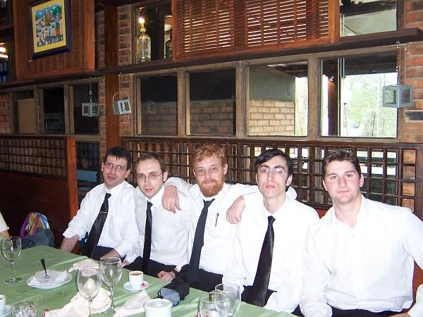 Cuatro músicos jóvenes en camisa blanca, sentados a una mesa antes de vestirse.