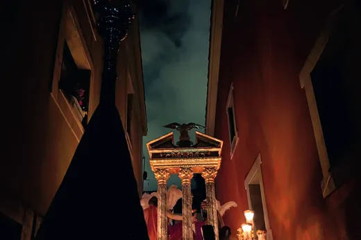 El paso avanza de madrugada por una calle estrecha, iluminado por su propia candelería.